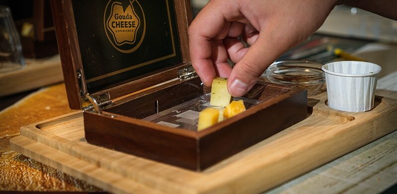 Visitor picks up a piece of cheese from a wooden tasting box at the Gouda Cheese Experience.