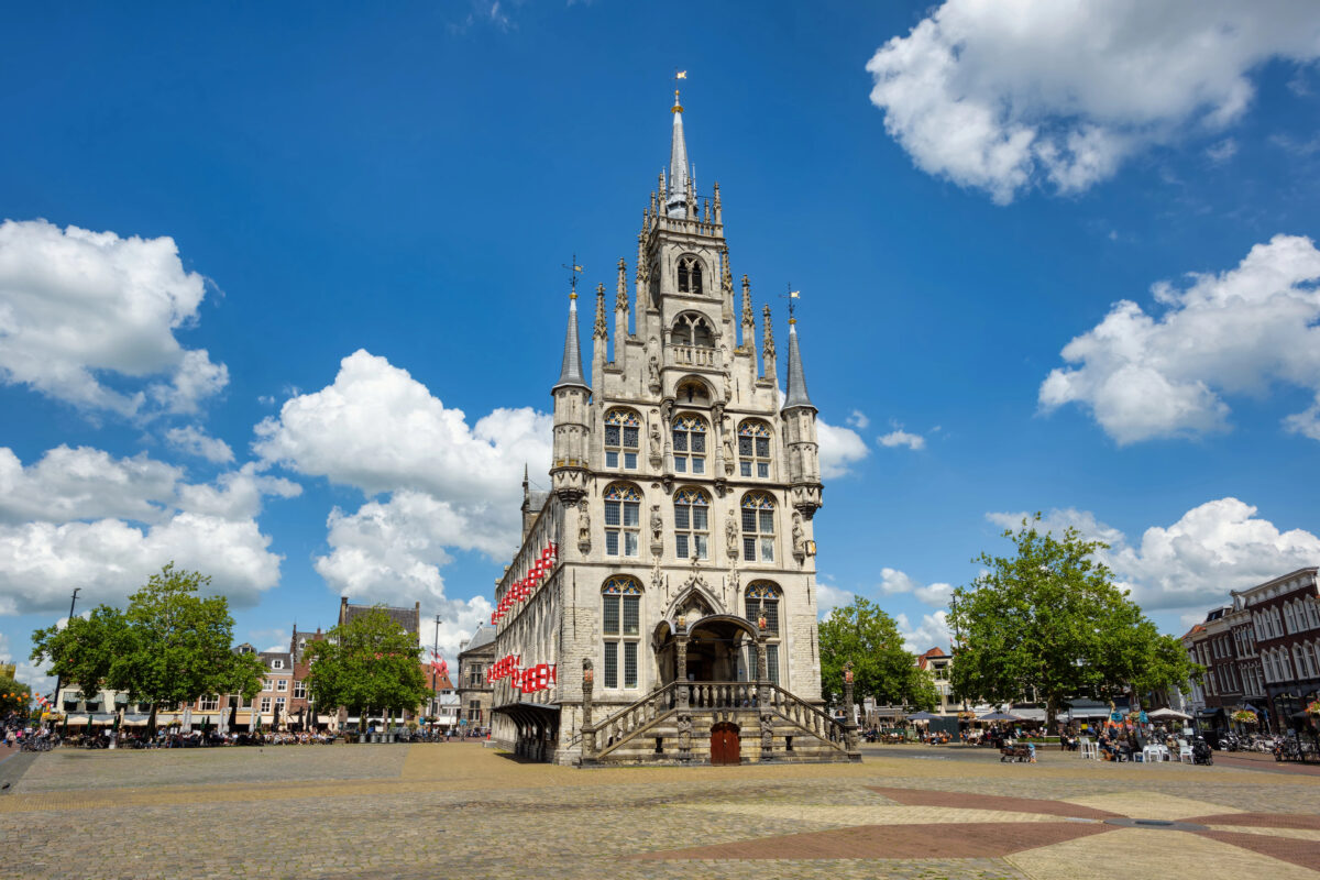 Het historische stadhuis van Gouda op de Markt, met blauwe lucht en terrasjes rondom.