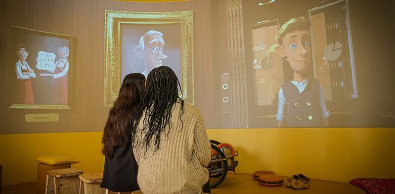 Twee bezoekers kijken naar een kunstzinnige animatie over kaas en historie in de Gouda Cheese Experience.