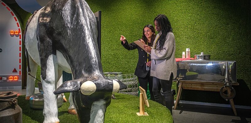 Twee bezoekers ontdekken een interactieve melkkoe tijdens een educatieve rondleiding bij de Gouda Cheese Experience.